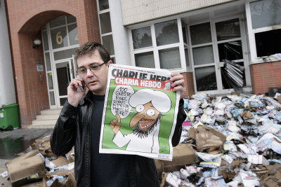 The Charlie Hebdo's publisher, known only as Charb, uses his cell phone as he shows a special edition of French satirical magazine Charlie Hebdo on November 2, 2011 in Paris, in front of the magazine's offices which were destroyed by a petrol bomb attack overnight. The fire at the weekly magazine started around 01.00 am (0200 GMT) and caused no injuries, a police source said. Charlie Hebdo published a special edition on November 2 to mark the Arab Spring, renaming the magazine Charia (Sharia) Hebdo for the occasion, to "celebrate" the Ennahda Islamist party's election victory in Tunisia and the transitional Libyan executive's statement that Islamic Sharia law would be the country's main source of law. The cover features a cartoon of the prophet, saying: "100 lashes if you don't die of laughter!". AFP PHOTO / ALEXANDER KLEIN (Photo credit should read ALEXANDER KLEIN/AFP via Getty Images)